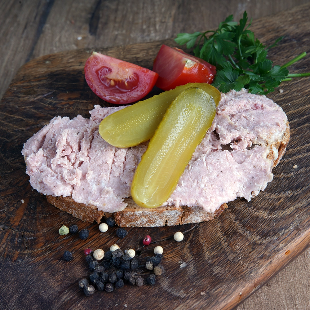 Eine Brotscheibe mit Gehacktem, garniert mit Gewürzgurken und Tomaten.